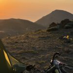 Zelt und bepacktes Bikepacking-Rad im Morgenlicht auf einem Bergrücken in Ostanatolien, dahinter Sonnenaufgang über dem Dunst des Vansees.