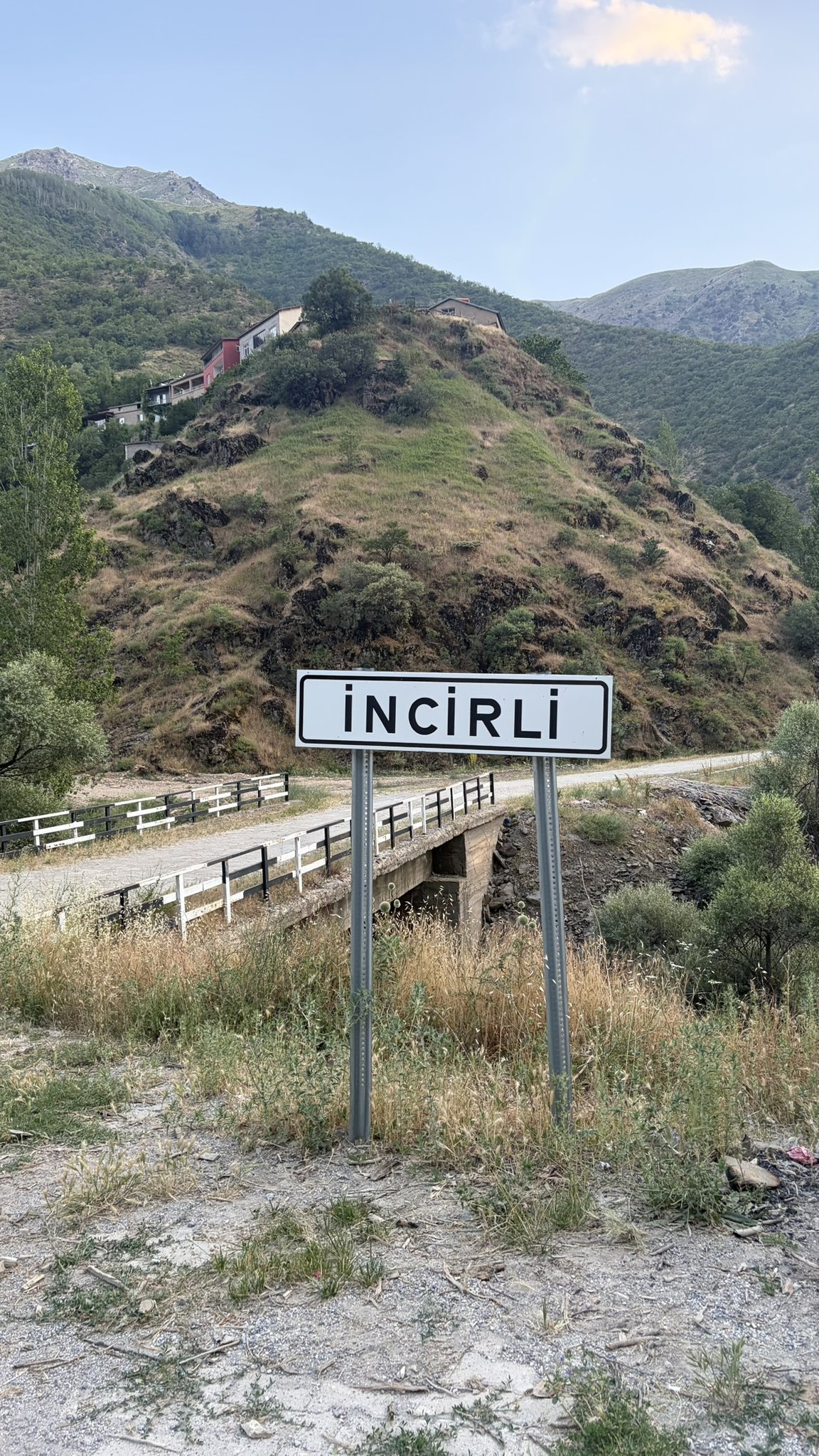 Ortsschild İncirli an einer Brücke, dahinter ein Dorf am Hang in den Bergen Ostanatoliens.